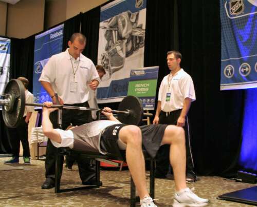 An athlete performs a bench press as two coaches observe at an NHL fitness combine event in Toronto