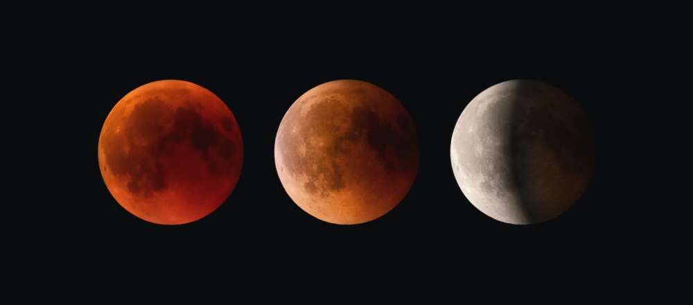 The moon during a different phases of a lunar eclipse. The first moon is full and red, the second (in the middle of the photo) is orange and partly in shadow, the last moon (to the right of the moon in the middle) is half in shadow and is white. All of the moons are set against a black background.