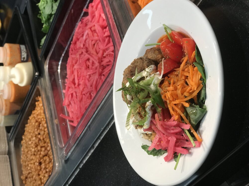 A bowl of salad sits in front of a salad bar.