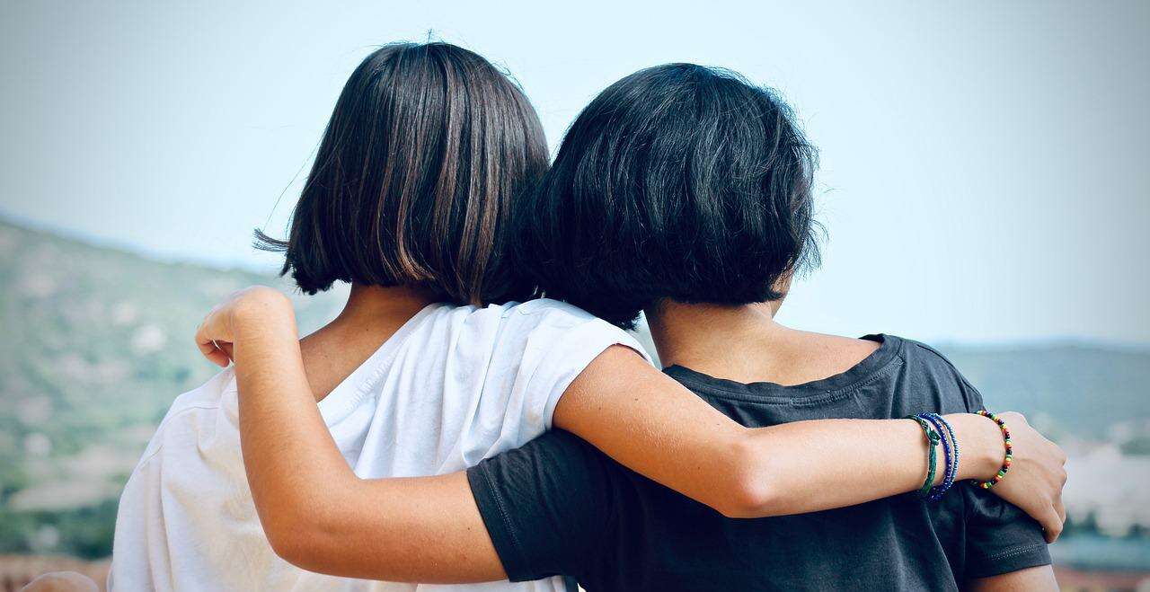 Two women are seen from behind with their arms over each others' shoulders