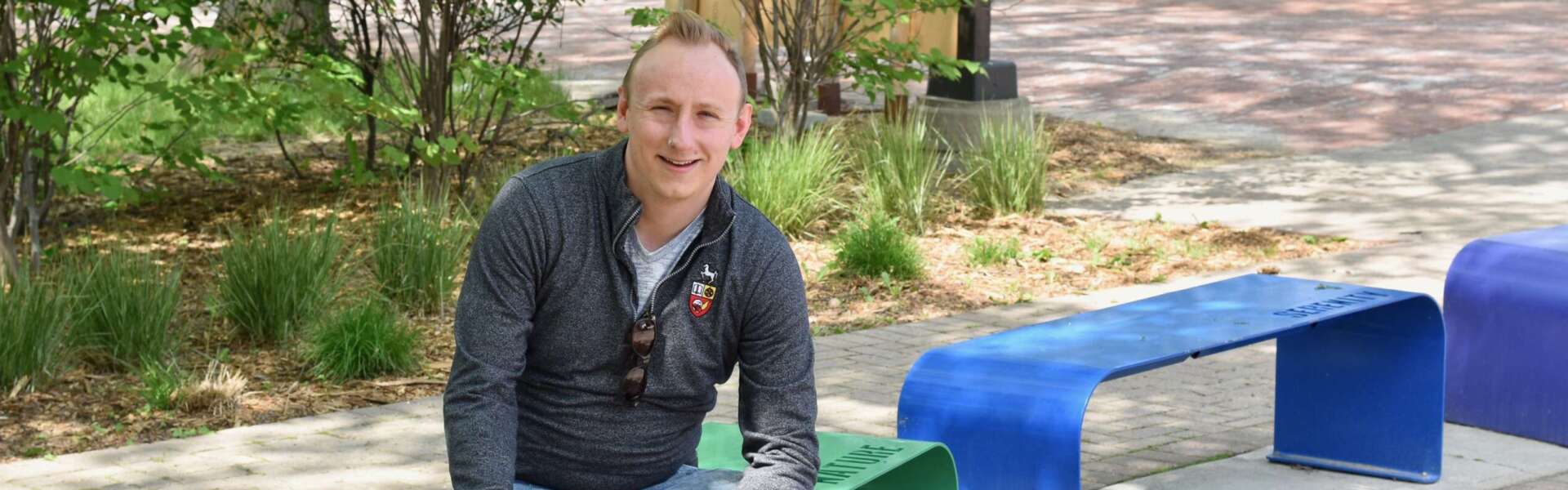 Dr. Adam Davies sits on rainbow-coloured benches at U of G.