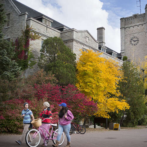Three U of G students walk across campus, one with a bike.