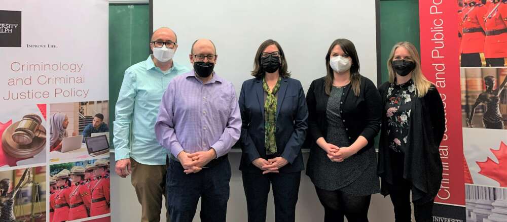 Five masked people stand in a row in front of a white board.
