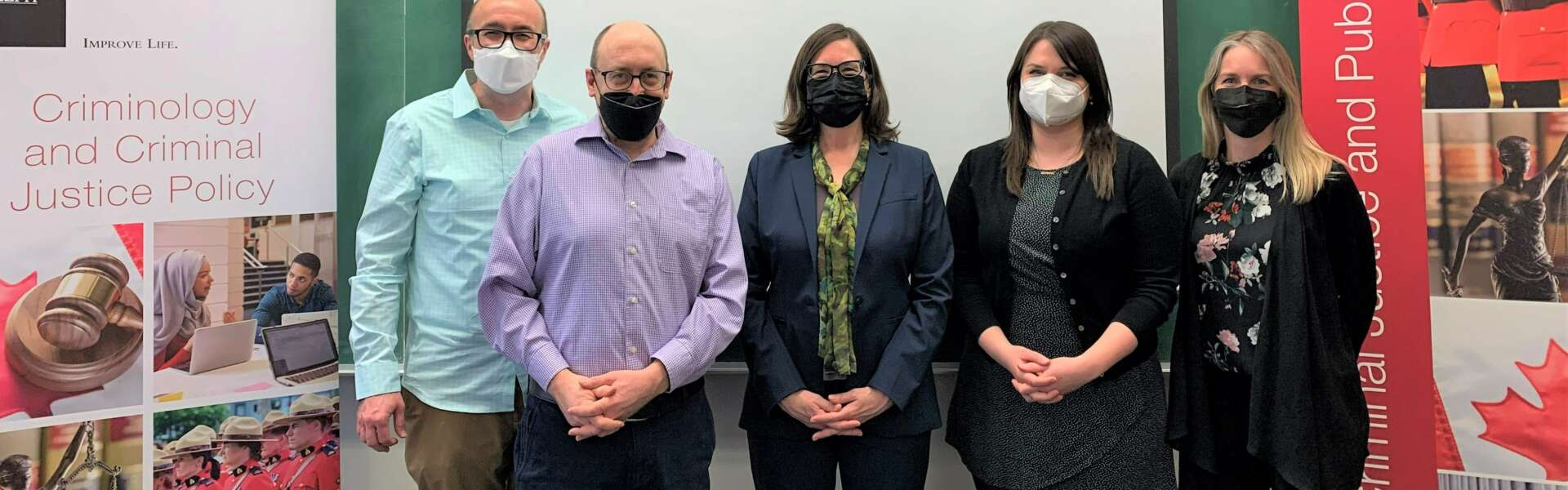 Five masked people stand in a row in front of a white board.