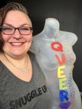 Dr. Ruth Neustifter poses for a photo next to a grey mannequin with "Queer" spelt out in a rainbow.