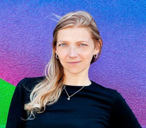 Dr. Susan Dupej poses for a headshot against a green, pink, purple and blue wall.