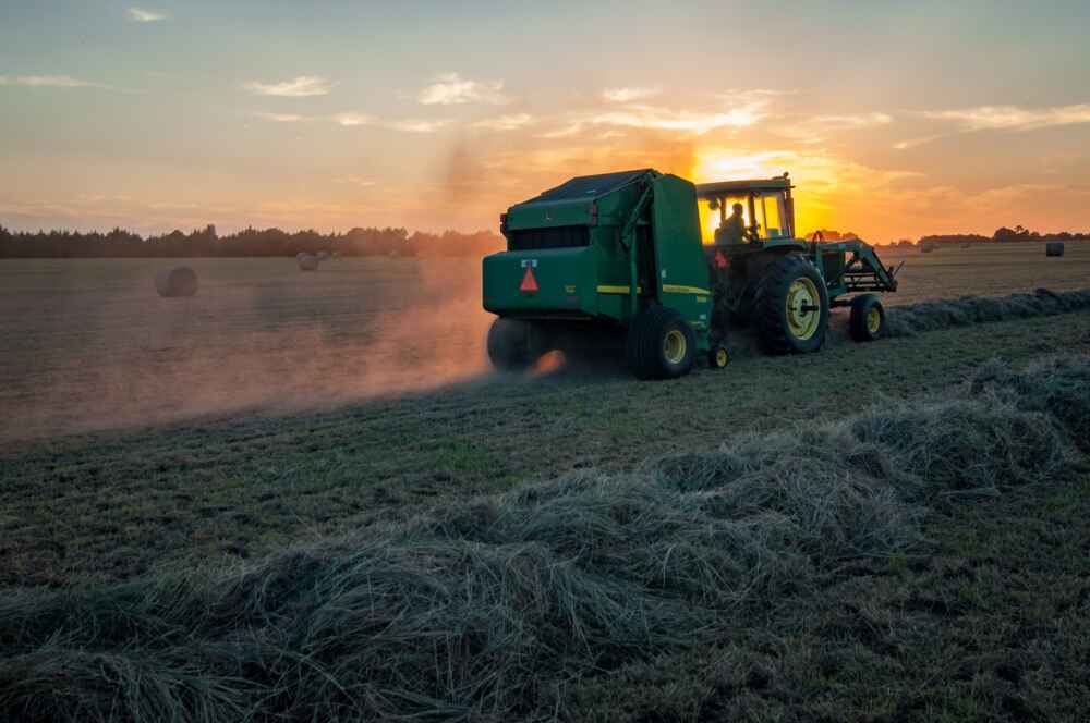 Farm equipmentstirs up dust on a field during sunset