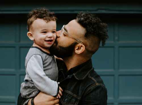 A man carries and kisses toddler on cheek