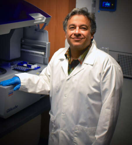 A man wearing a lab coat and gloves smiles at the camera