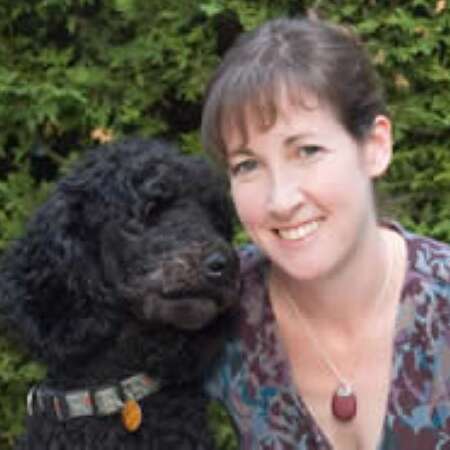 Dr. Shannon Gowland in front of green bushes. On her left is a black dog.