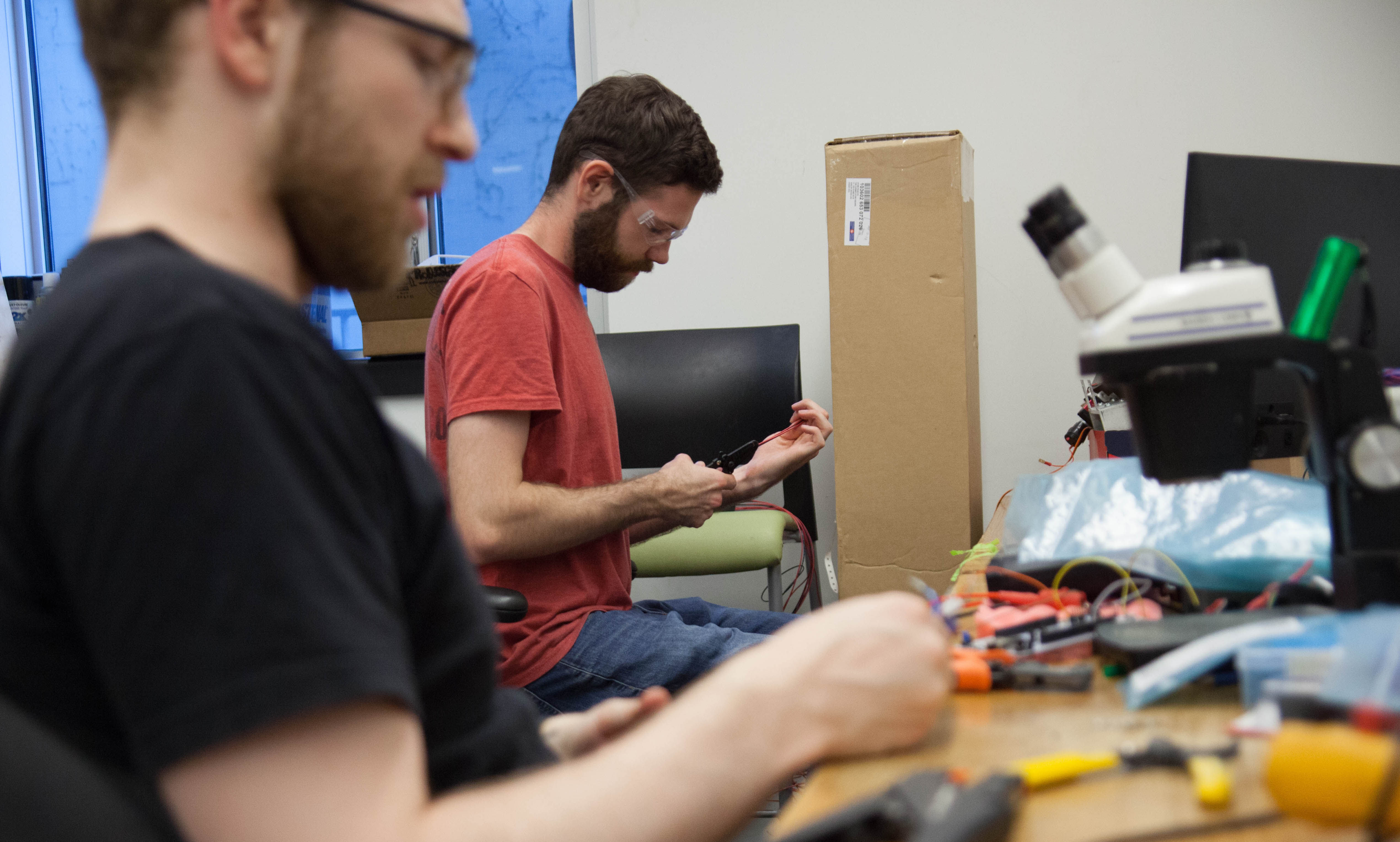 two people sit a desk and use tools to adjust wiring