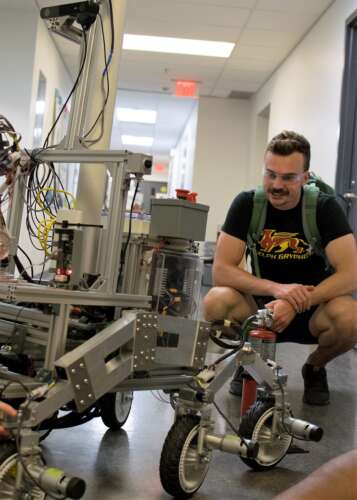Team member Spencer Ploeger crouches down to examine the rover