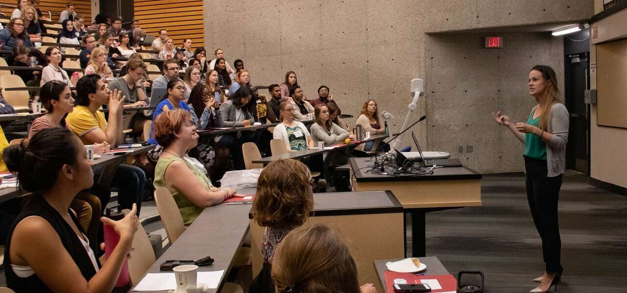 a teacher gestures while standing in front of a large lecture hall