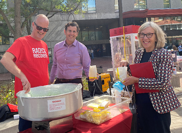 Dr. Mike von Massow, Ontario Agricultural College, Dr. Ben Bradshaw, AVP Grad Studies, and U of G president Dr. Charlotte Yates gather around a table laiden with food outside a building.