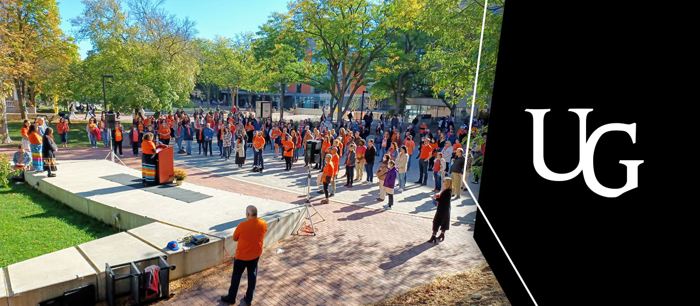 A large crowd of people many wearing orange shirts gather in U of G 's Branion Plaza on a sunny fall day