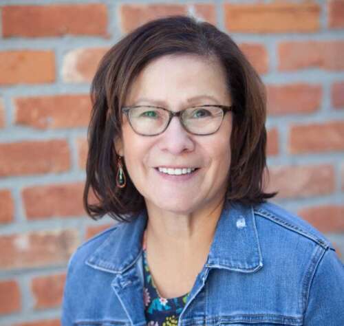 A woman wearing a jean jacket stands near a brick wall