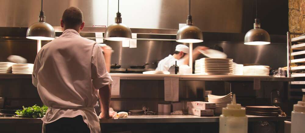 a waiter stands near an open kitchen where chefs work