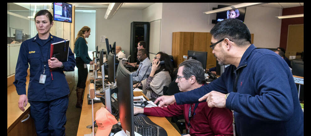 Several people look at computers, and answer phones in a health crisis centre