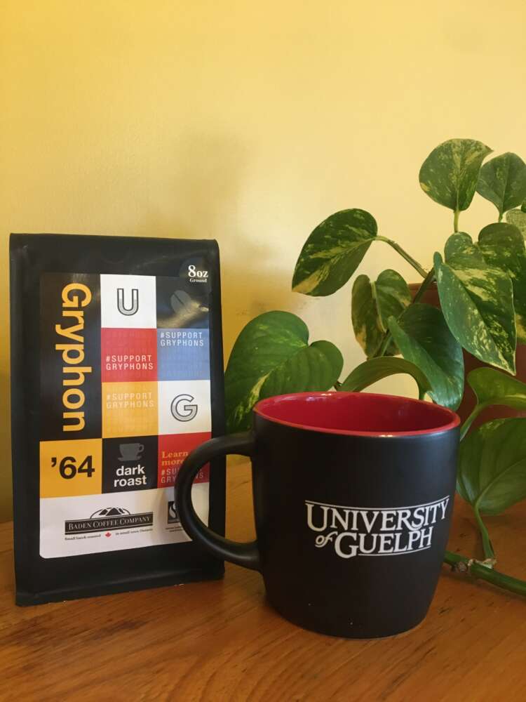 A University of Guelph mug sits in front of a package of coffee and a green plant.