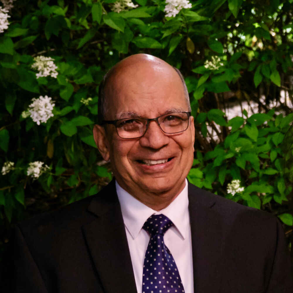 Dr. Ramesh P. Rudra smiles in front of a flowering bush.