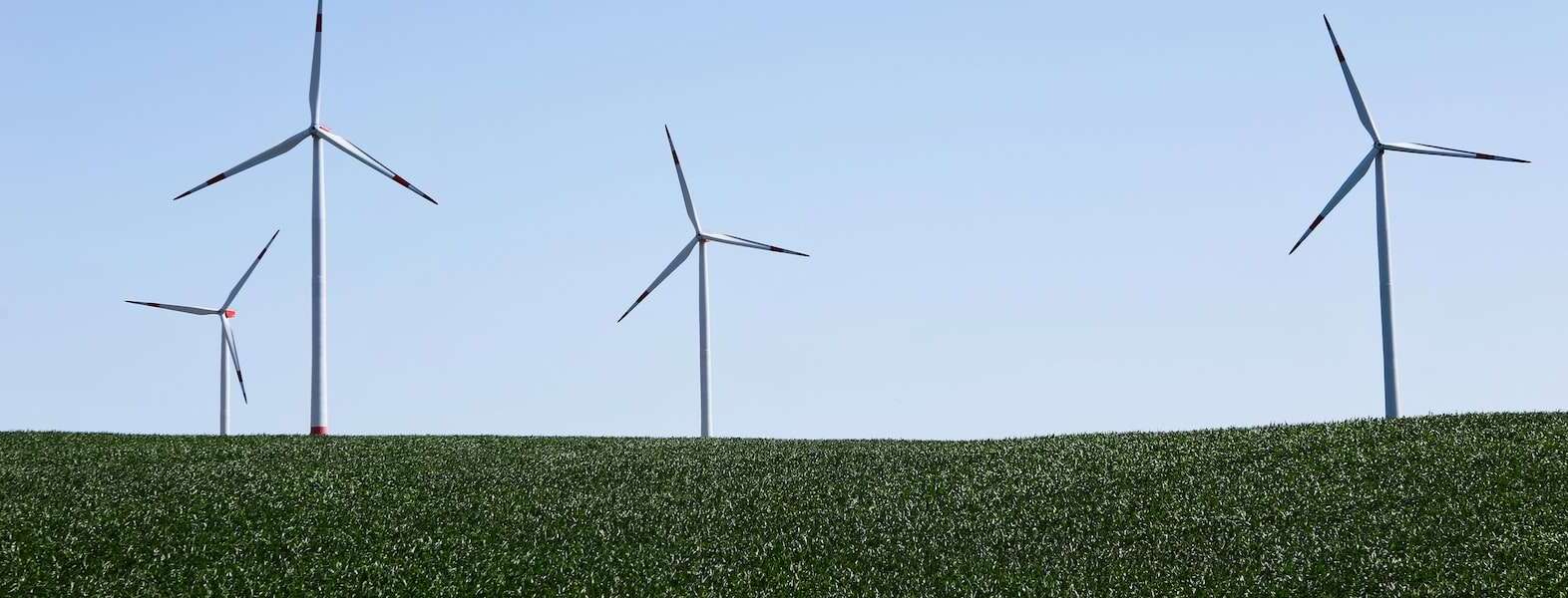 Four wind turbines in a green field against a blue sky.