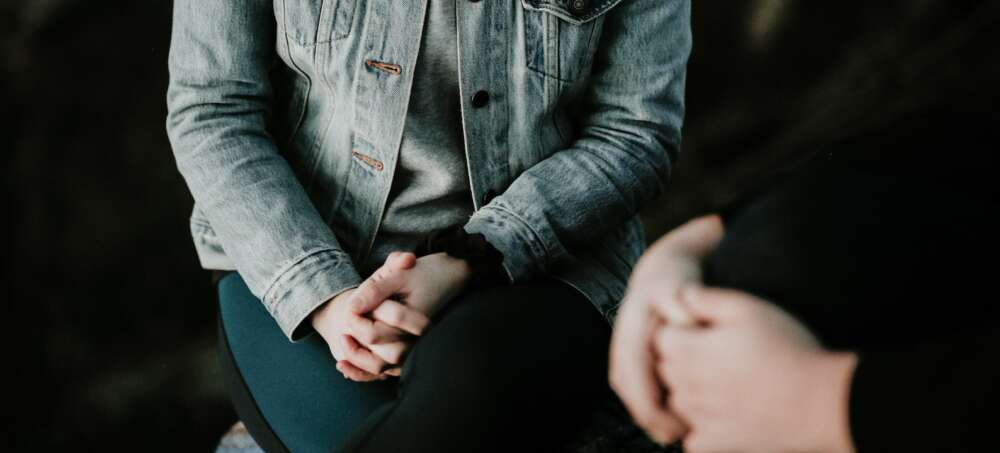 Person wearing jean jacket with ahands folded near another with hands folded