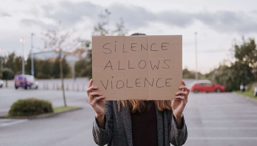 Unrecognizable woman in casual clothes standing on road and demonstrating poster Silence Allows Violence