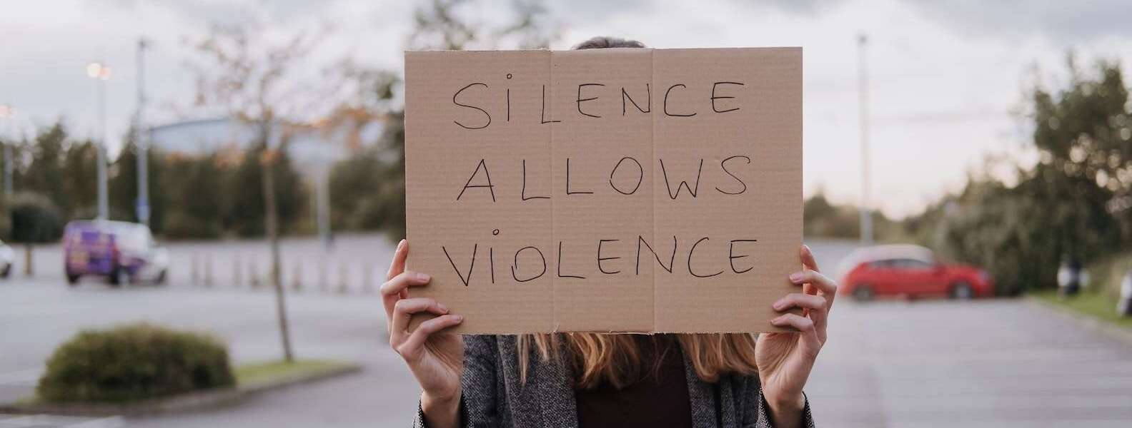 Unrecognizable woman in casual clothes standing on road and demonstrating poster Silence Allows Violence