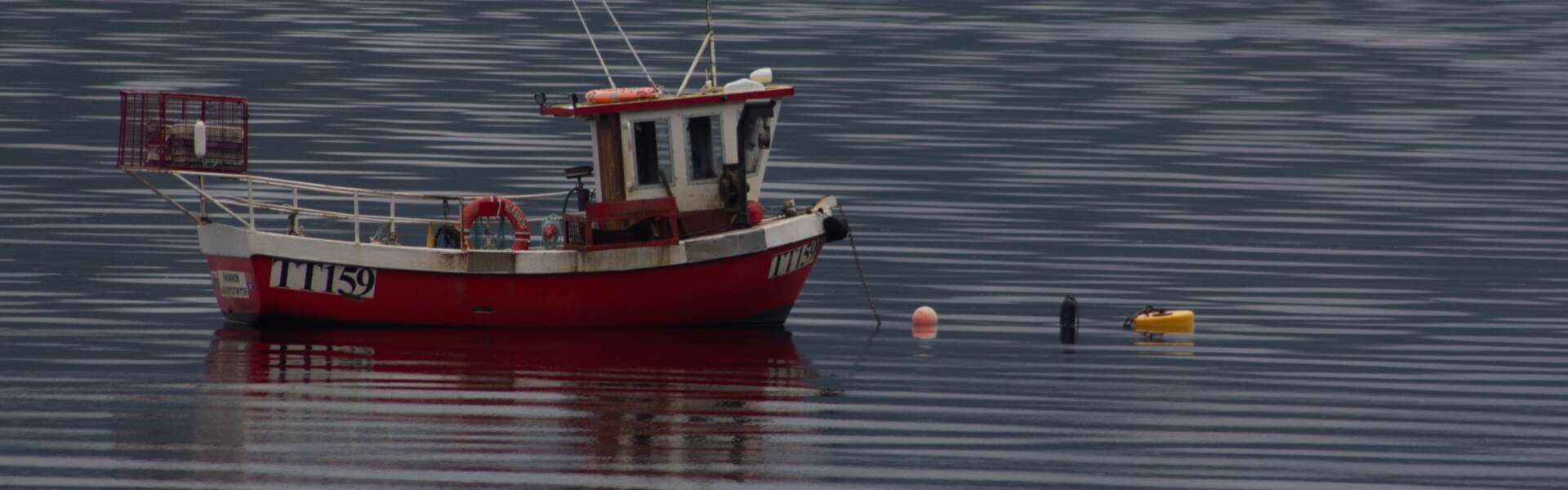 A small red and white fishing boat with fishing gear laid out in front of it sits in a body of water