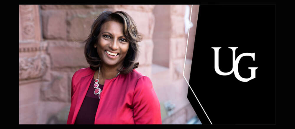 Indira Naidoo-Harris stnads against a sandstone building and smiles for the camera