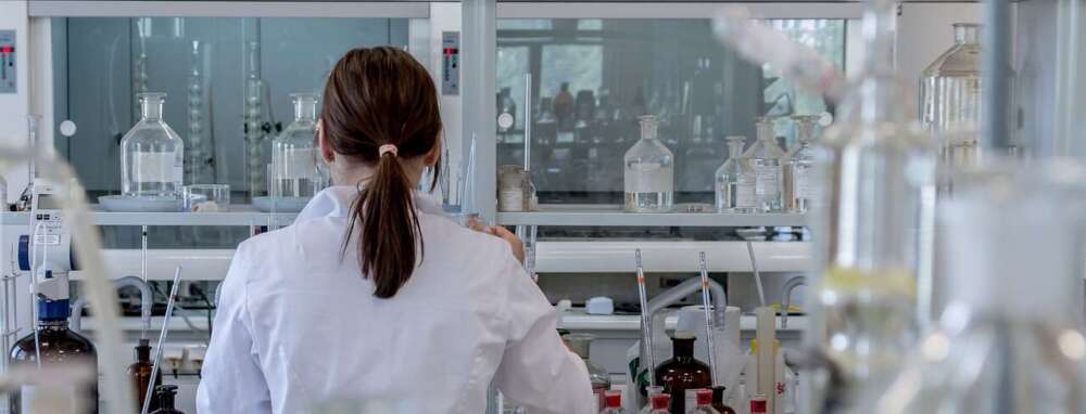 A woman wearing a white lab coat and her hair in a ponytail, works in a science lab