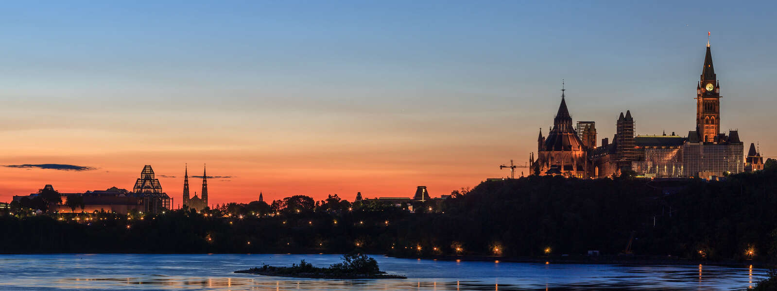 Parliament Hill and the Ottawa skyline are silhouetted at sunrise behind the Rideau River