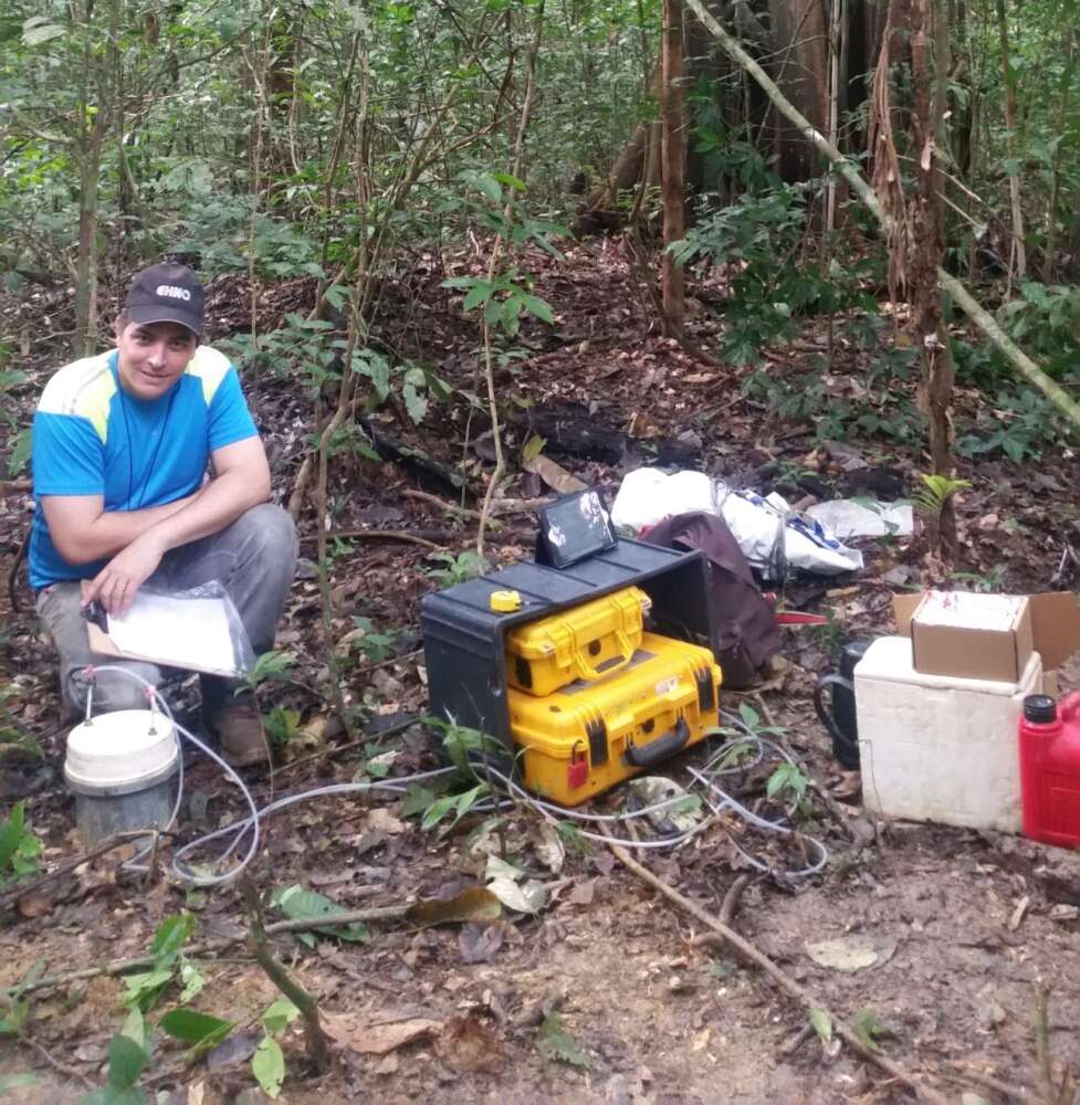 Dr. Dasiel Obregon poses next to equipment for soil testing in a clearing of the Amazon Rainforests