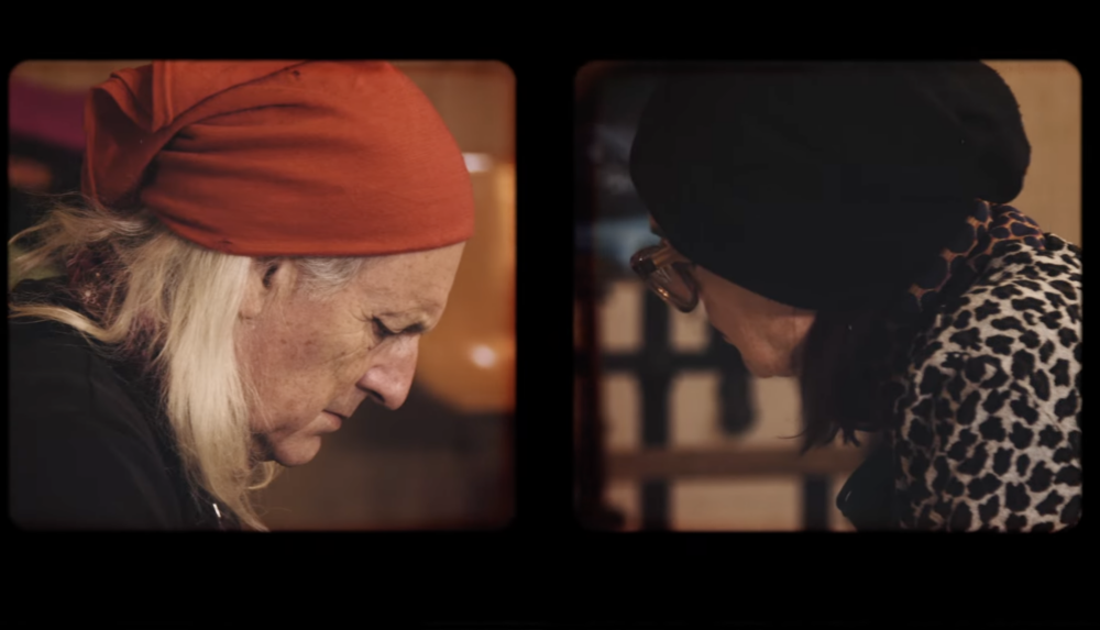 Person in red bandana facing right concentrates on work while opposite them is a person in a black head scarf and glasses facing down.