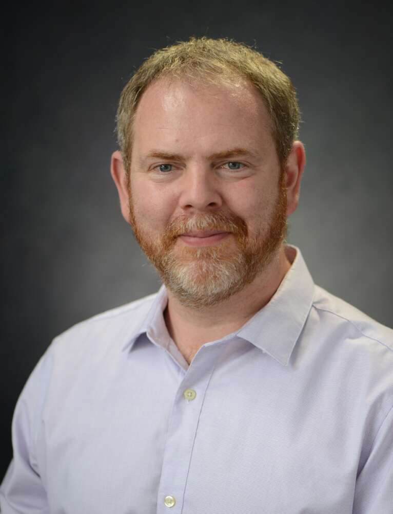 Dr. Nigel Raine poses for a photo in front of a grey backdrop