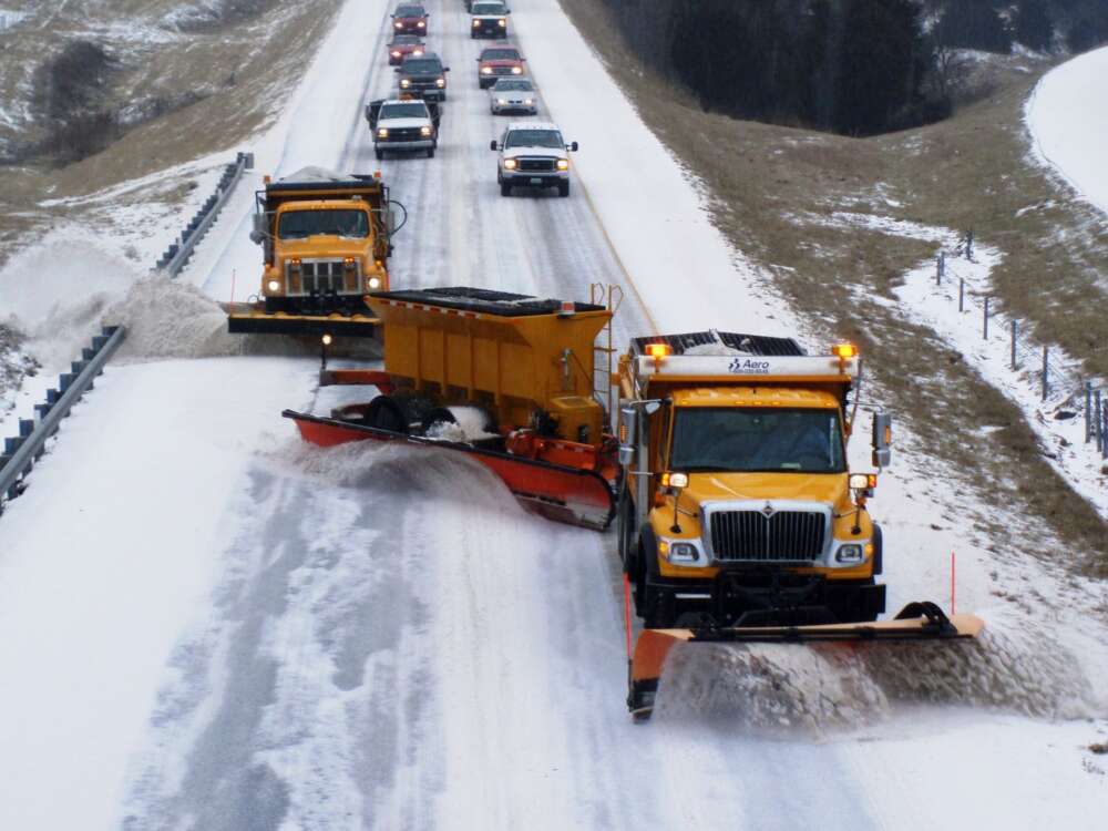 Three yellow snow plows lead traffic on a snowy road