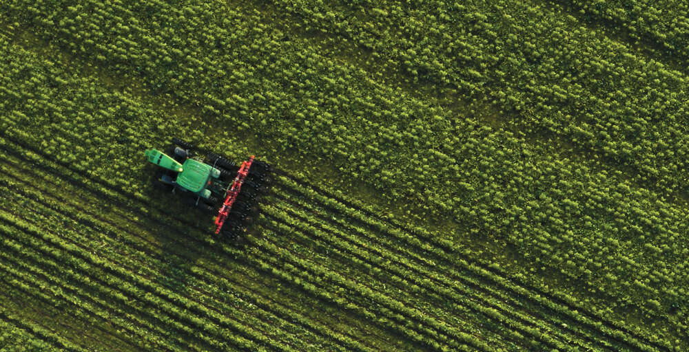 An aerial shot of a tractor moving diagonally across a green fiedl