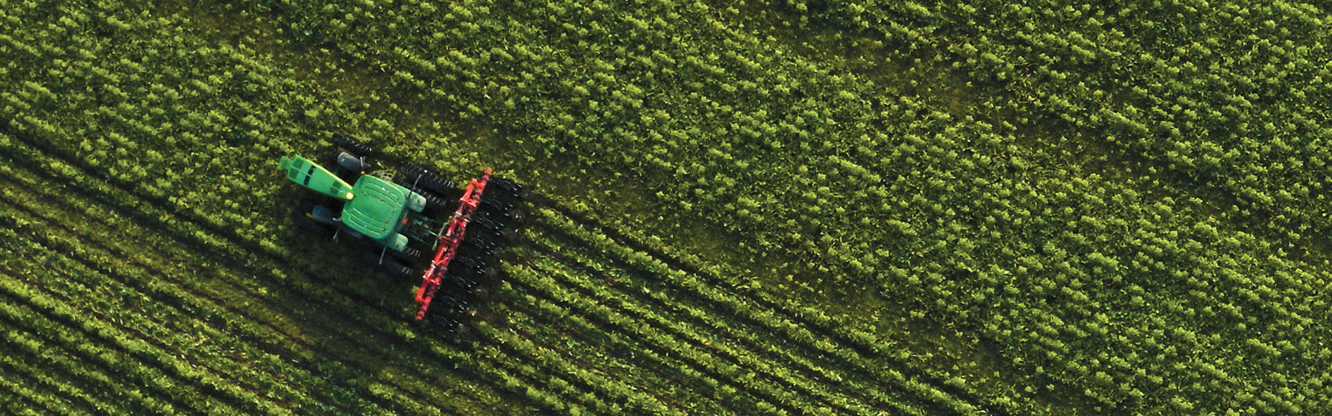 An aerial shot of a tractor moving diagonally across a green fiedl