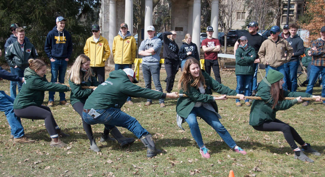 Participants pull on a rope during a tug-a-war competition outdoors while onlookers watch from behind