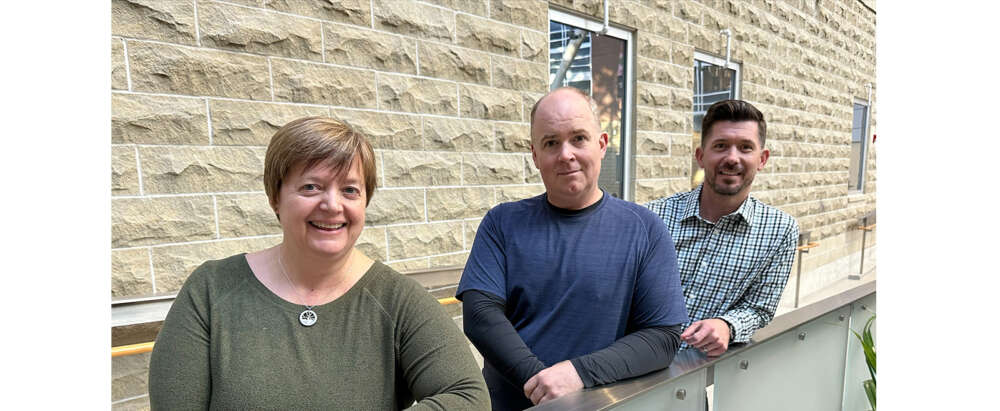 Three people stand near a wall in the Summerlea Science Complex atrium