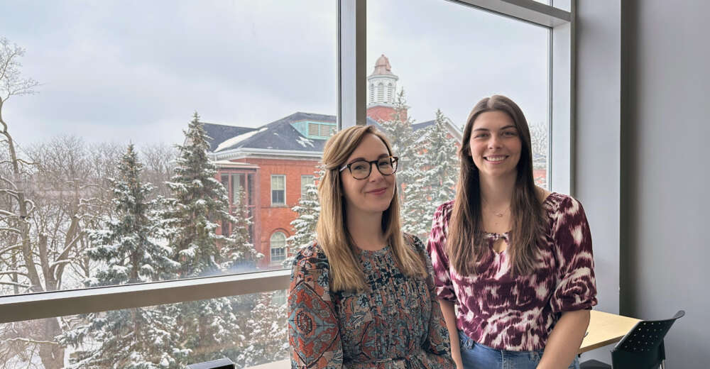two women at a window with snow-covered trees behind