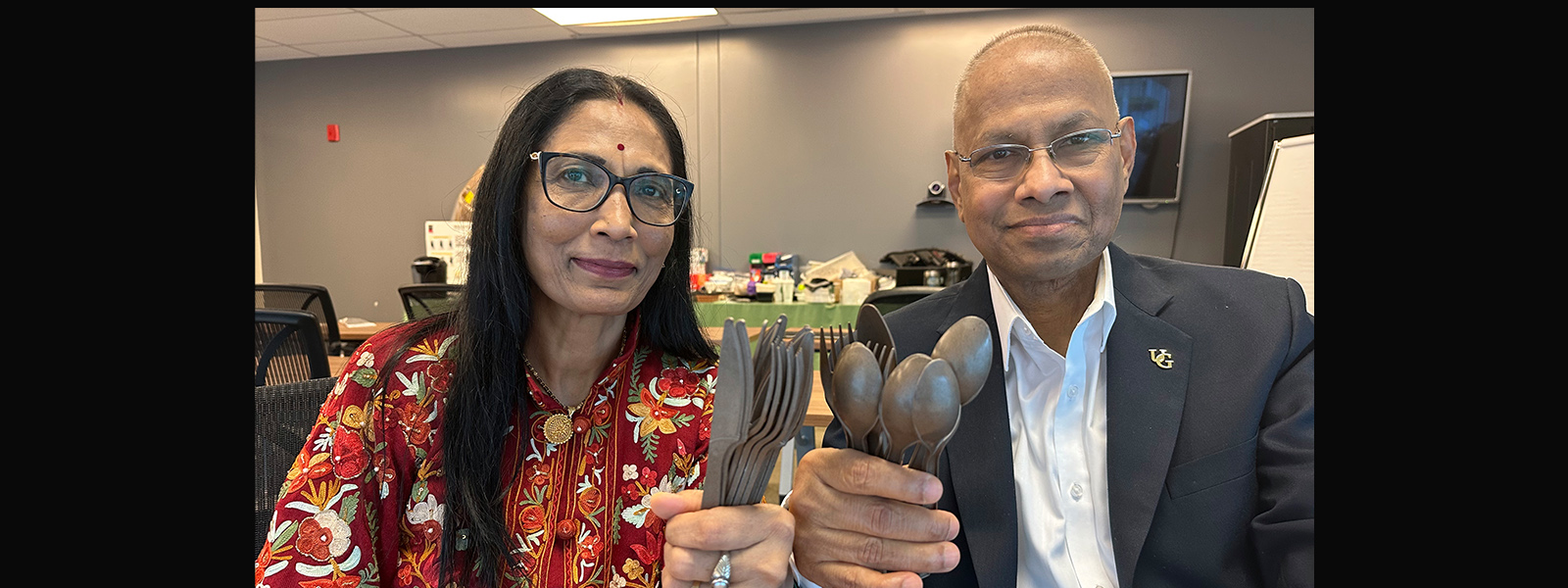 Two people hold up bioplastic cutlery and smile for the camera