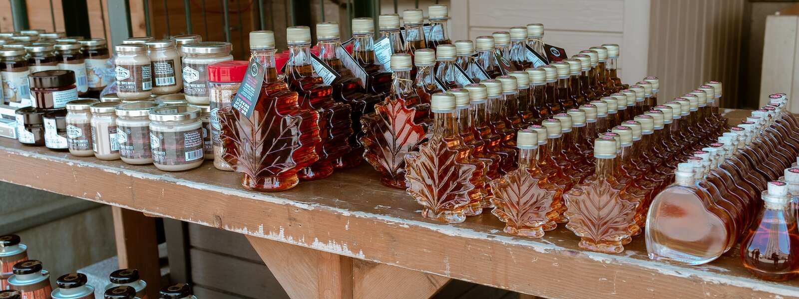 assorted glass bottles of maple syrup on wooden shelves