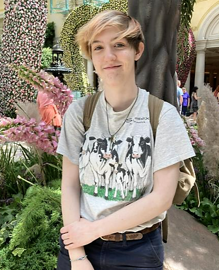 A person smiles for the camera while posing in front of an indoor garden