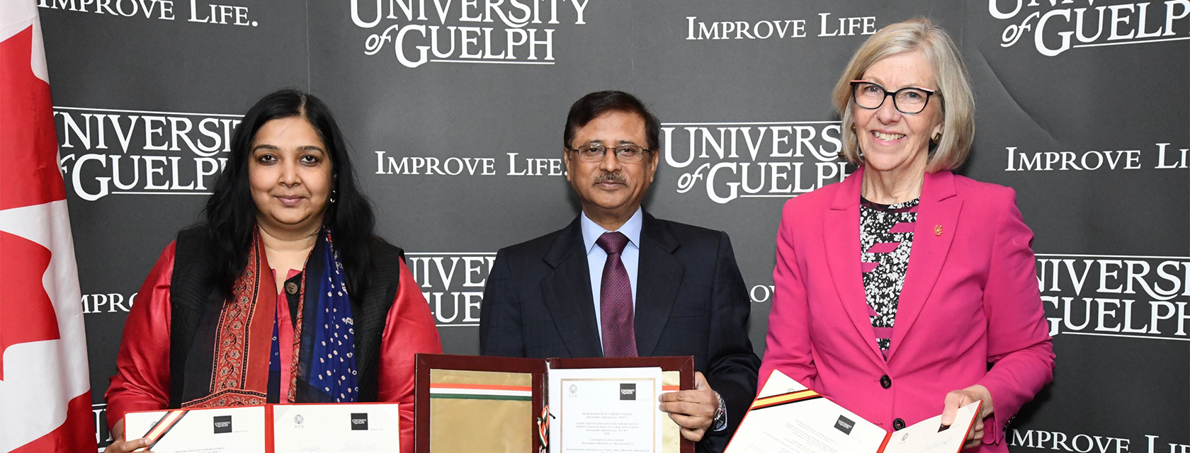 Three people hold out folders containing signed letters in front of a University of Guelph logo background