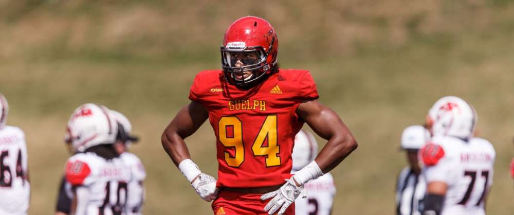 a football player in a red Gryphons uniform surveys the fiedl with other players behind him