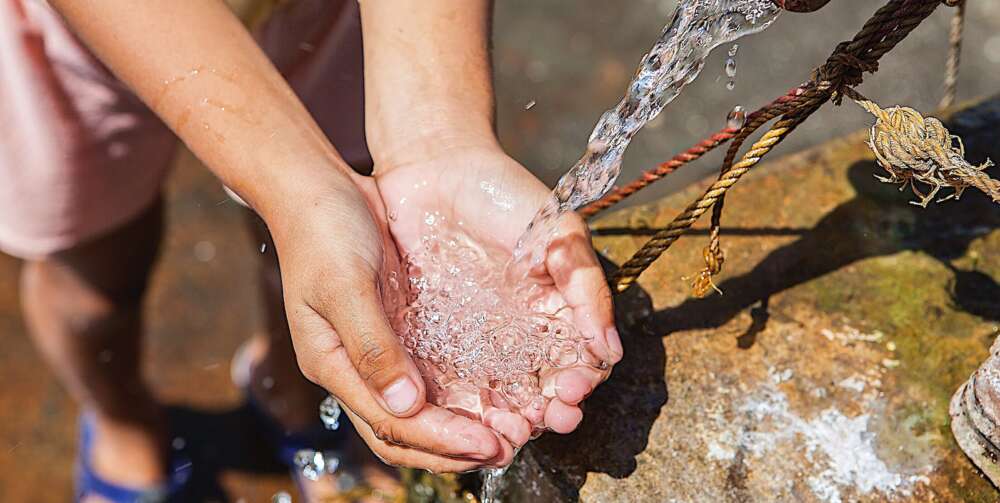 outstretched hands gather water from a water pump