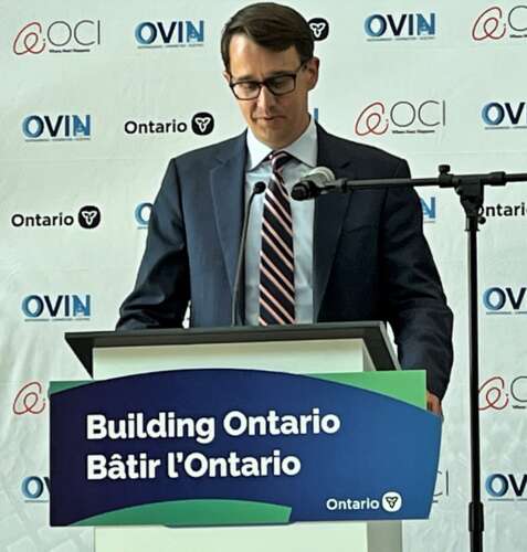 a person stands at a podium bearing the sign "Building Ontario" in English and French and speaks into a microphone