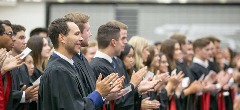a line of students in convocation regalia smile and applaud