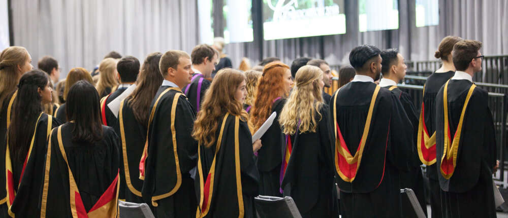 a line of graduands in convocation regalia are shown from behind